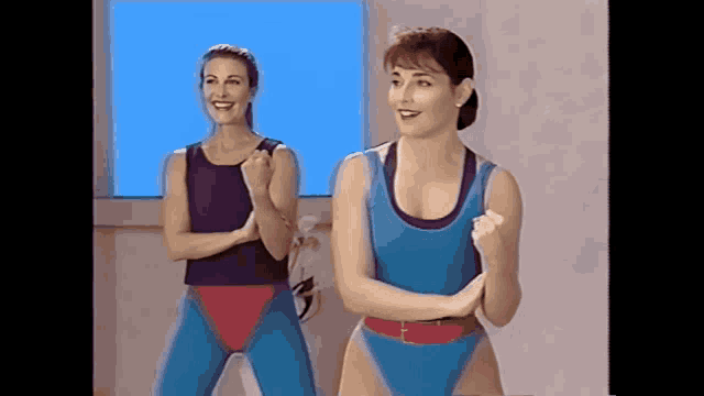 two women wearing blue leotards are dancing in front of a window