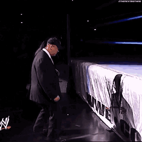a man in a suit and hat is standing next to a sign on a wrestling ring .
