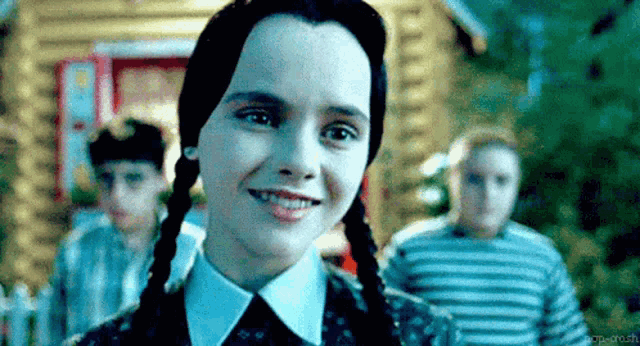 a close up of a girl with pigtails smiling in front of a group of children .