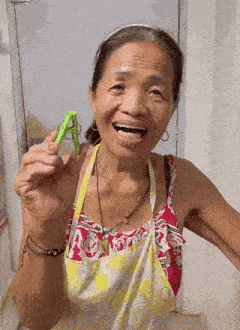 an elderly woman in an apron is holding a green clothespin in her hand .