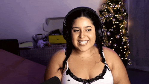 a woman wearing headphones and a bra is smiling in front of a christmas tree