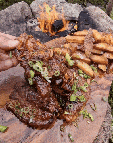 a steak and french fries on a wooden cutting board with a fire in the background