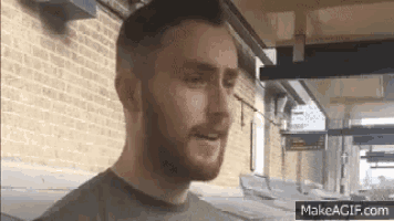 a man with a beard is standing in front of a brick wall and talking to someone .