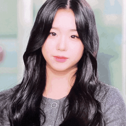 a woman with long black hair is wearing a gray sweater