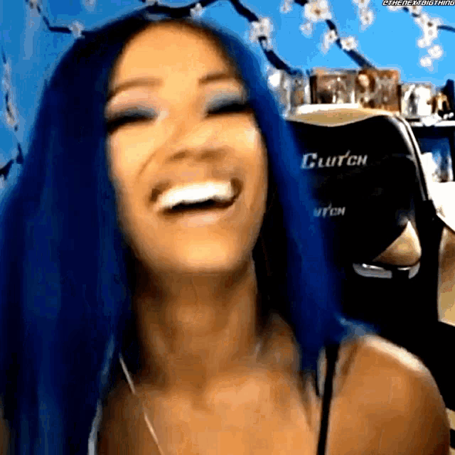a woman with blue hair is laughing in front of a chair that says clutch on it .