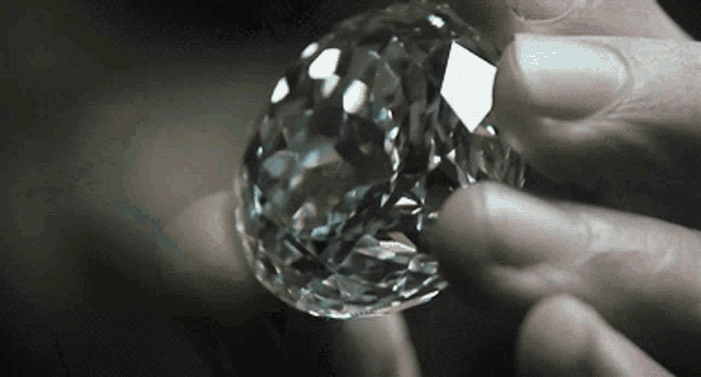 a close up of a person holding a large diamond in their hands