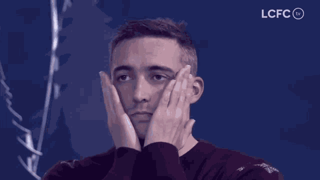 a man covering his face with his hands with the lcfc tv logo in the background
