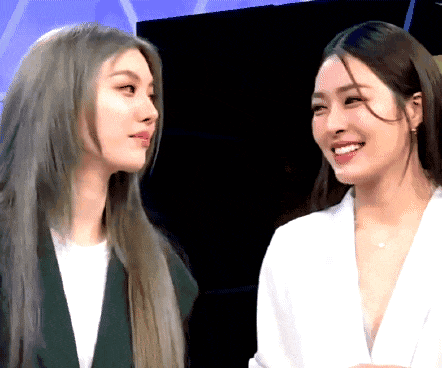 two women are looking at each other and smiling while standing next to each other