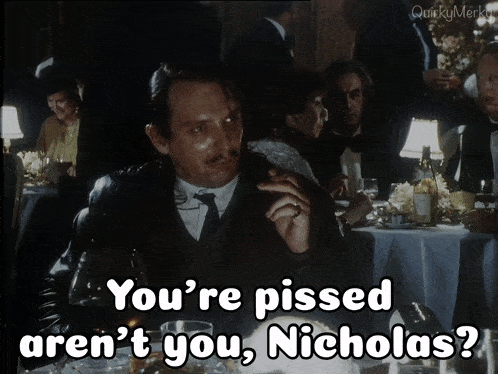 a man sitting at a table with the words " you 're pissed aren 't you nicholas " above him