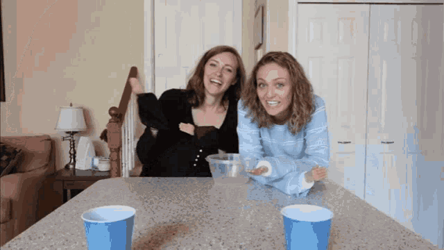two women are sitting at a table with blue cups on it