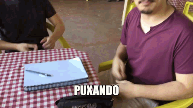 a man sits at a table with a notebook and a pencil case with the word puxando on it