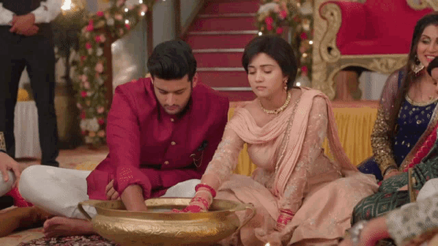 a man and a woman sit on the floor with a bowl of water in front of them