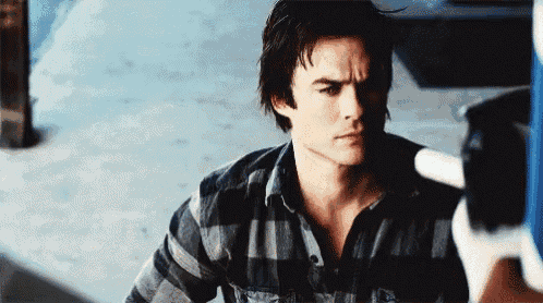a man in a plaid shirt is standing next to a car and holding a hammer .