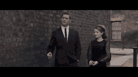 a man in a suit and tie is standing next to a woman in a black dress against a brick wall .