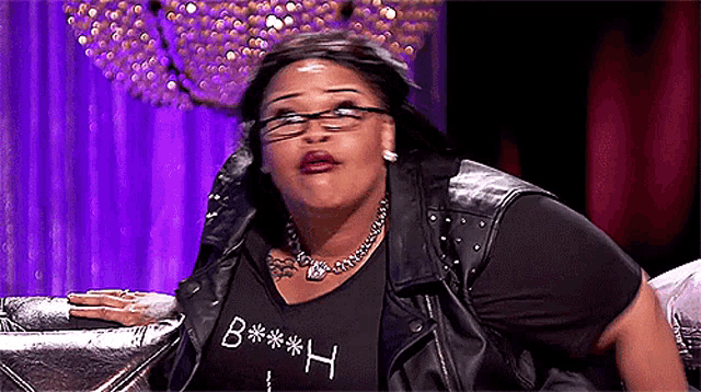 a woman wearing glasses , a leather jacket , and a black shirt with the letter h on it .
