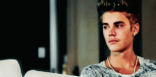 justin bieber is sitting on a couch looking at a laptop computer .