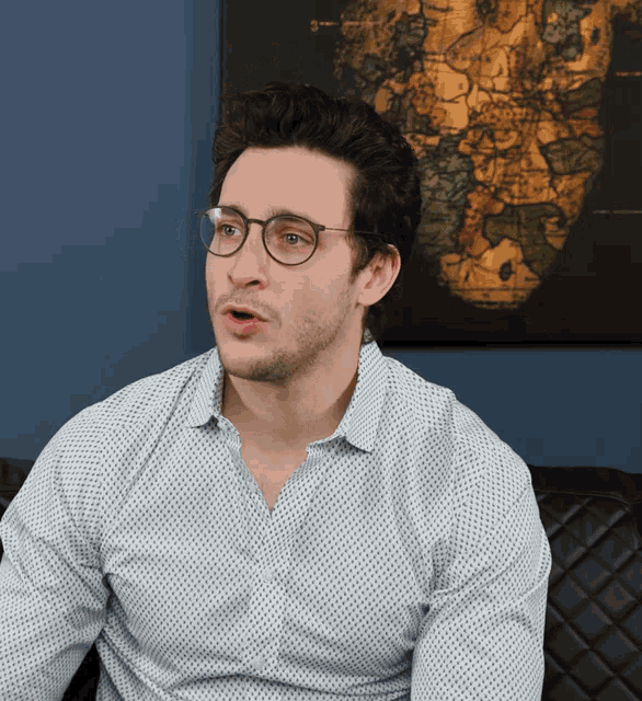 a man wearing glasses and a white shirt is sitting in front of a map of africa