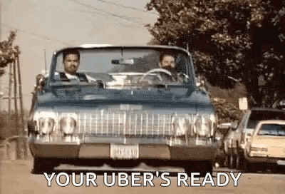 two men are driving a car down a street with the words `` your uber 's ready '' written on the side .