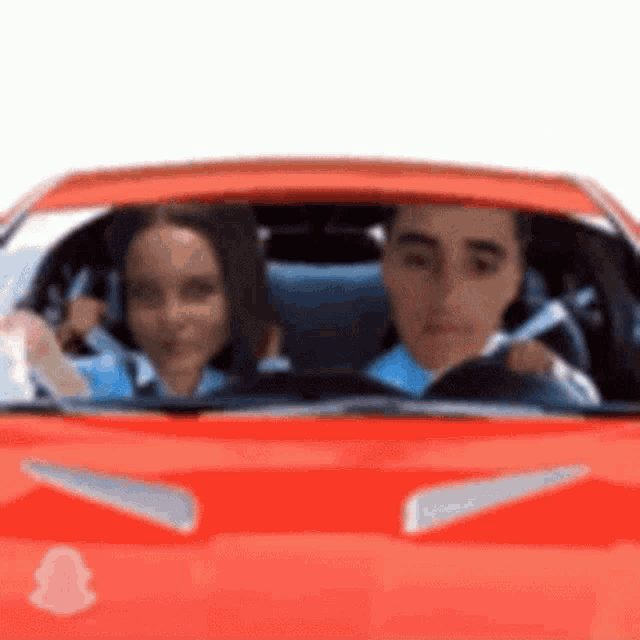a man and a woman are driving a red sports car