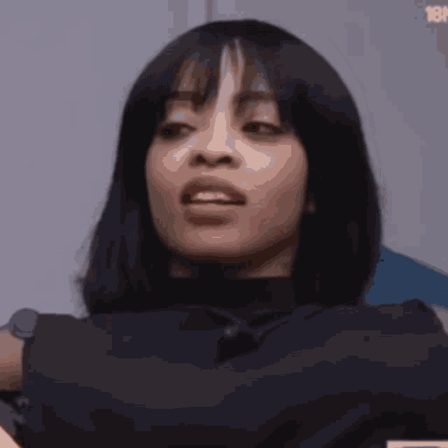 a woman with short black hair and bangs is making a funny face while wearing a black shirt .