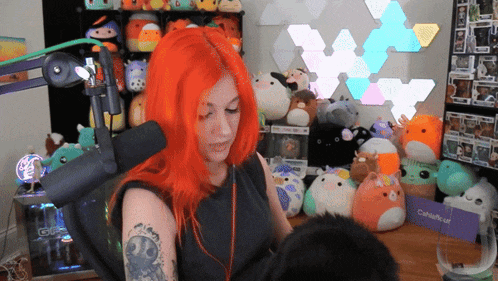 a woman with red hair is sitting in front of a microphone in a room filled with stuffed animals and toys