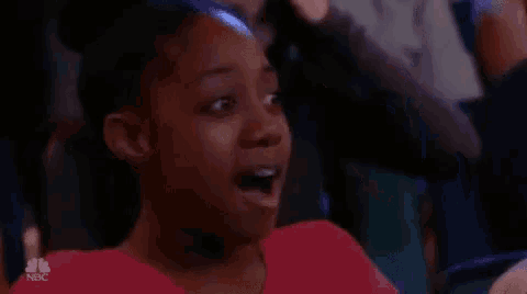 a young girl is sitting in a theatre with her mouth open and a surprised look on her face .
