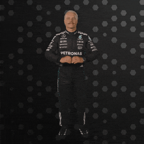 a man in a petronas suit stands in front of a dark background
