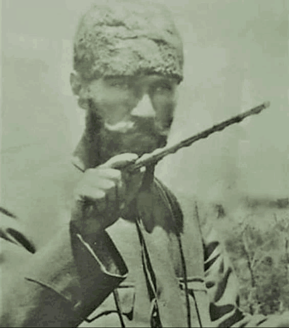 a black and white photo of a man with a beard holding a stick .