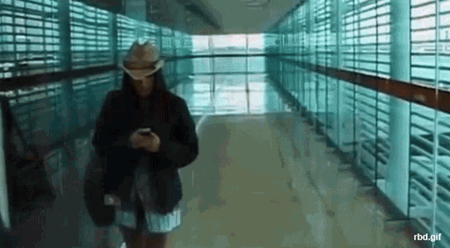 a woman in a cowboy hat is walking down a hallway looking at her cell phone .