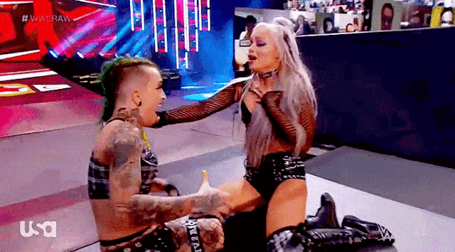 two women are wrestling on a stage and one of them is holding the other 's hand .