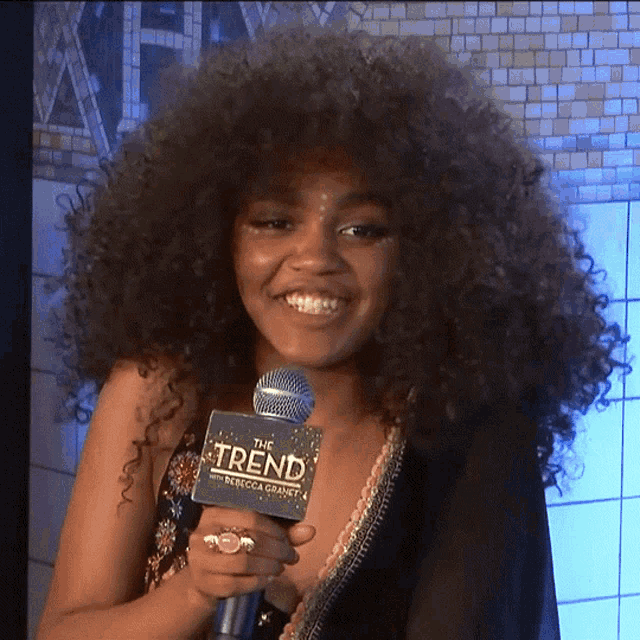 a woman with curly hair is holding a microphone that says the trend on it