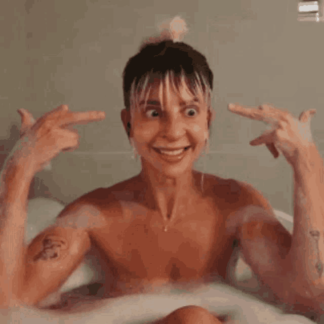 a shirtless man is taking a bath and pointing at himself with his fingers .