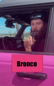 a man is driving a pink bronco with a sign on the door that says bronco