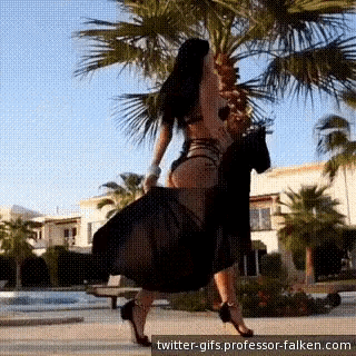 a woman in a black dress is standing in front of palm trees