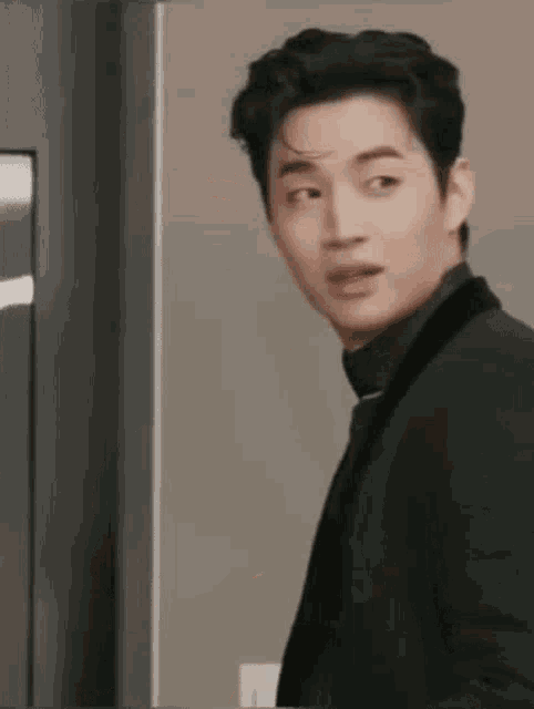 a young man in a suit and tie is standing in front of a refrigerator .