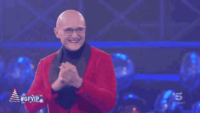 a bald man wearing glasses and a red jacket applauds in front of a sign that says #gfvip