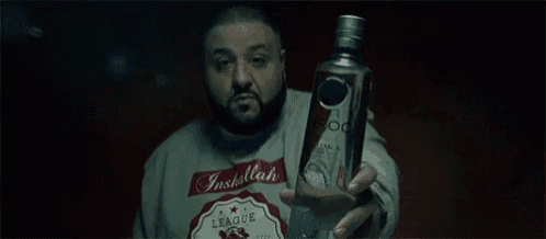 a man in a sweater is holding a bottle of vodka in his hand .