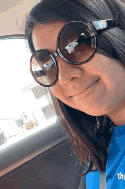 a woman wearing sunglasses and a blue shirt that says " the "