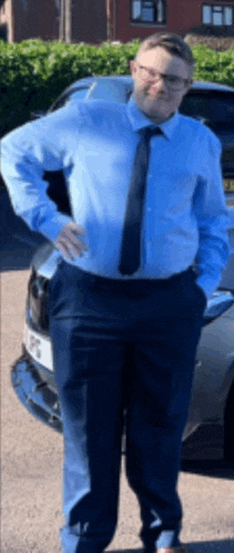 a man in a blue shirt and tie stands in front of a car