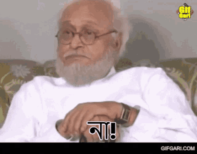 an older man with glasses and a beard is sitting on a couch with a watch on his wrist .