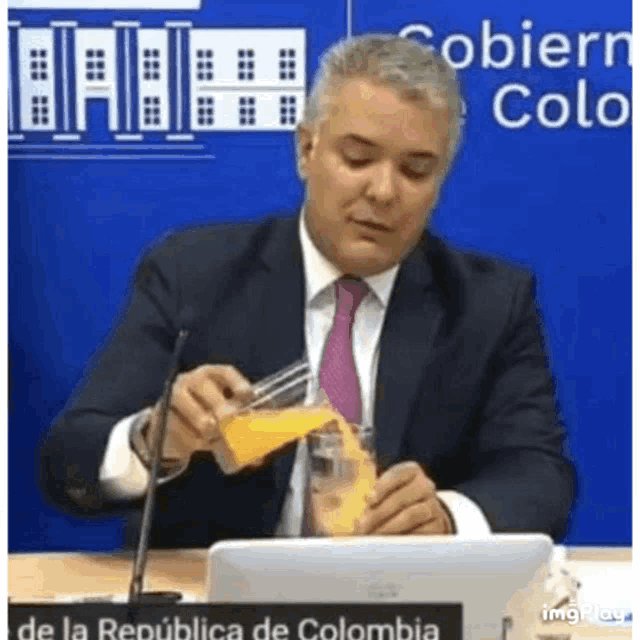 a man in a suit and tie is pouring orange juice into a cup