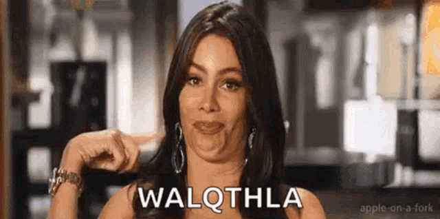 a woman is making a funny face and pointing at the camera with the word walqthla on her face .