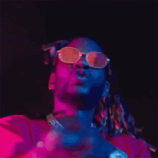 a man wearing sunglasses and a red shirt is standing in a dark room .