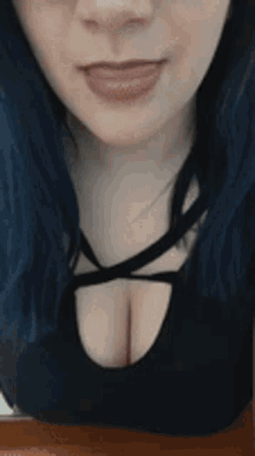 a woman with blue hair is wearing a black top with a cut out in the front .