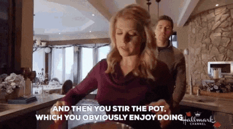 a woman is stirring a pot of food in a kitchen while a man stands behind her .
