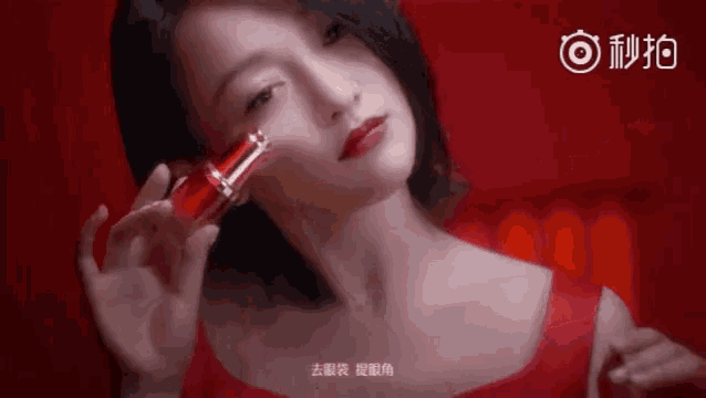 a woman in a red top is holding a bottle of red lipstick