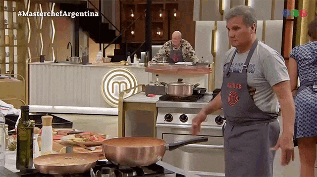 a man wearing an apron with the letter m on it stands in front of a stove