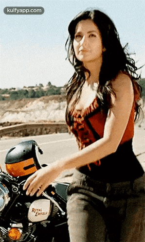 a woman is standing next to a royal enfield motorcycle on the side of a road .