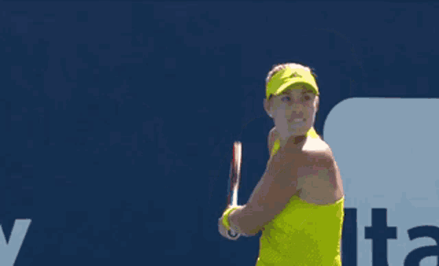 a woman in a yellow tank top is swinging a tennis racket at a ball
