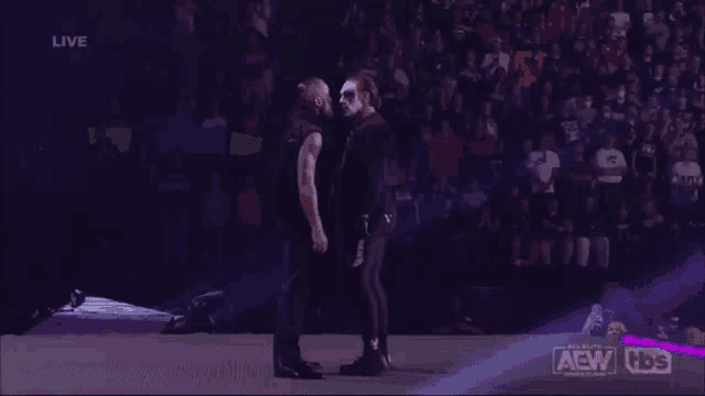 a couple of wrestlers are standing next to each other on a stage in front of a crowd .